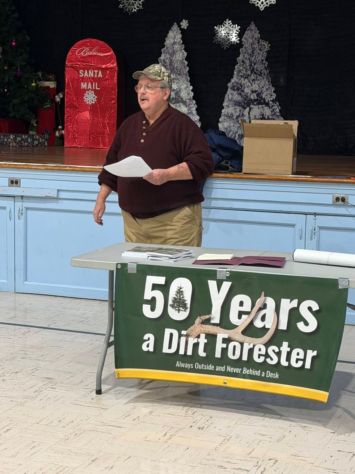 William Sargent reading from his book behind a table with a 50 Years a Dirt Forester banner